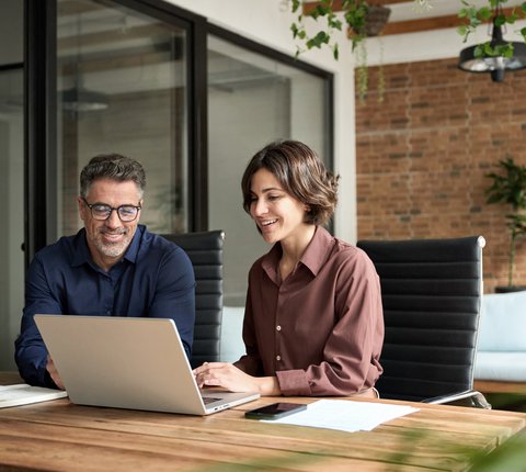 Zwei Mitarbeitende arbeiten gemeinsam an einem Laptop in einem modernen Büro- und Besprechungsraum.